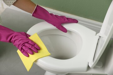 Woman cleaning toilet seat in restroom, closeup