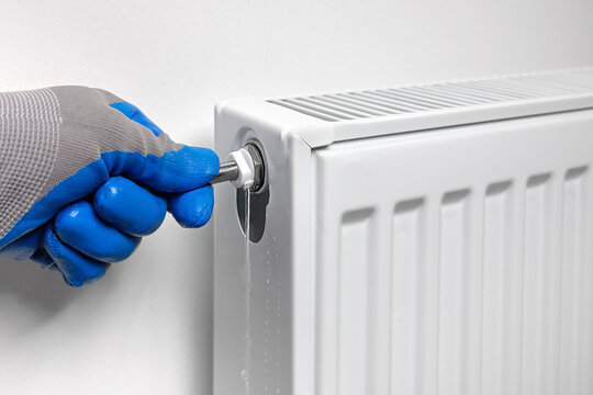 A plumber uses a key to drain air, draining water and air from a radiator in an apartment.