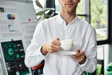 A focused redhead businessman sips coffee, deep in thought about a project in his stylish office.
