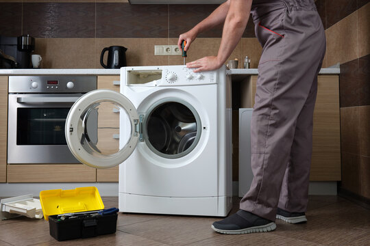 A adult household appliance repairman disassembling a washing machine with a screwdriver.