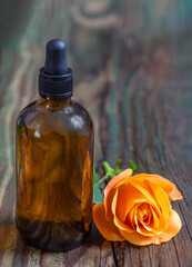 Romantic aromatherapy. Pink fresh blossom rose essential oil in dark glass bottle. wooden bacground