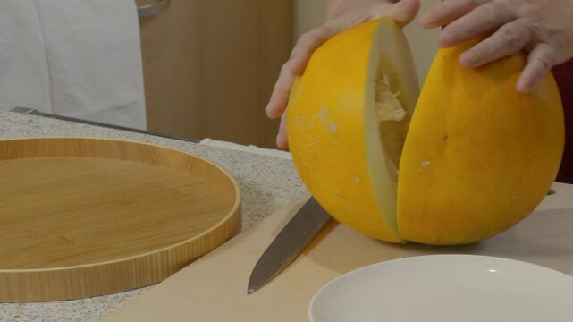 Woman's hand cuts a melon with a knife and removes the seeds with a spoon