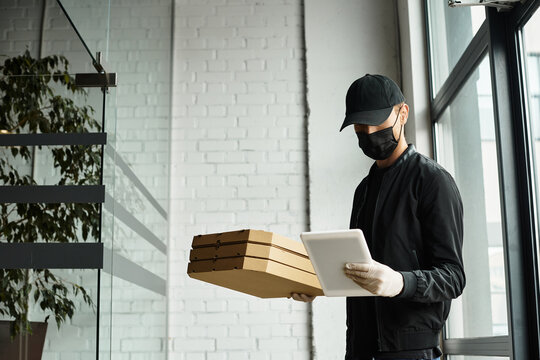 A delivery professional in a black mask carries food boxes into a modern office setting. - Powered by Adobe