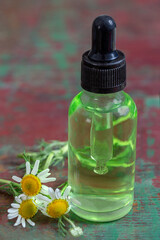 Small glass bottle with essential roman chamomile oil on the old wooden background. Chamomile flowers, close up. Aromatherapy, spa and herbal medicine ingredients. .