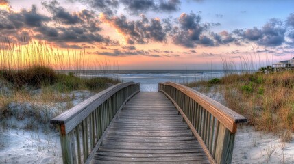 Fototapeta premium A tranquil wooden walkway approaches the beach as the sun sets, casting warm hues over the ocean and highlighting the grassy dunes