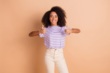 Portrait of pretty young girl show thumb up wear striped t-shirt isolated on beige color background