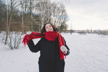 A smiling woman with a red scarf enjoys a snowy winter day in a serene forest setting beneath a...
