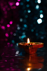 Glowing Diwali diyas with beautiful light reflection on the ground with bokeh effect in dark background.