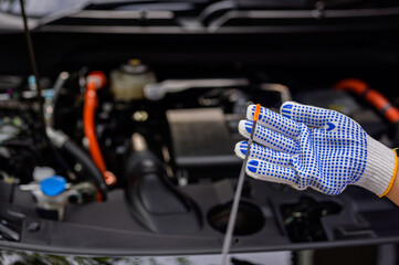 A mechanic in an auto repair shop checks the engine oil level for customers who use cars for...