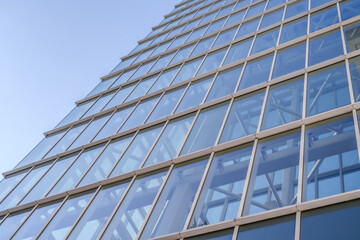A modern glass building rises into the sky, showcasing its grid-like facade and reflecting the clear blue atmosphere. The architectural lines create a sense of depth and symmetry.