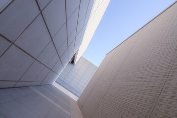 Geometric architecture creates a narrow passageway with towering, sleek walls under a clear blue...