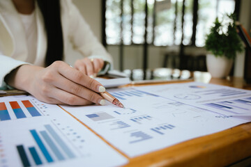 A businesswoman sits at her desk, calculating financial data on her laptop. Surrounded by paperwork and charts, she analyzes expenses and income, reflecting her role in corporate finance and accountin