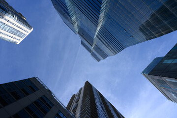 Skyscrapers tower above, converging towards a bright blue sky, creating a dramatic and imposing perspective. 