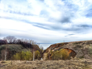 Scenic landscape with rolling hills and a calm body of water under cloudy skies during early spring in a serene natural setting
