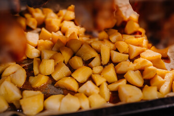 Close-up of roasted potato pieces in a baking tray, seasoned and cooked to golden perfection, with flavorful drippings visible on the parchment paper..