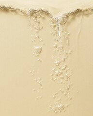 Close-up of flowing liquid with bubbles over a creamy beige surface, highlighting a smooth and...