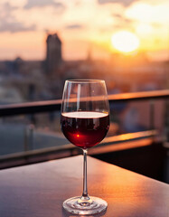 A glass of red wine on a balcony at sunset with city panorama. Selective focus.