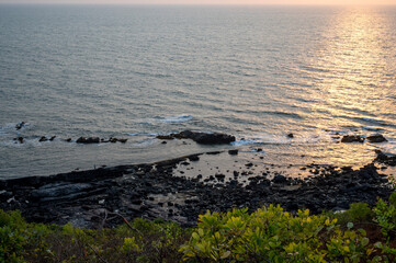 Close-up coastal view from Vagator Beach hilltop in Goa, India. Warm sunset light reflects on the...