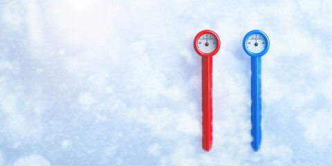 Red and blue thermometers measuring temperature of snow on sunny day