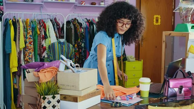 Young woman selling clothes and accessories online from home. Fashionable girl owning a small online business in her colored apartment. 