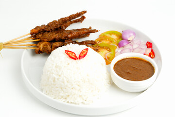 Rice and chicken or beef satay on the white plate with peanut sauce, tomato, onion and chili