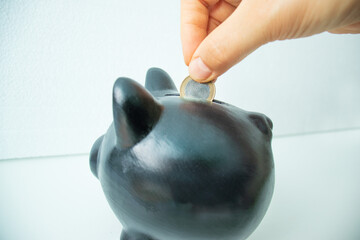 putting coins into a black piggy bank, piggy bank,  Saving money for future plans and retirement fund