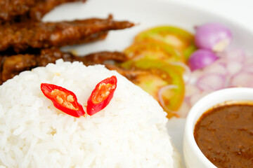 Rice and chicken or beef satay on the white plate with peanut sauce, tomato, onion and chili