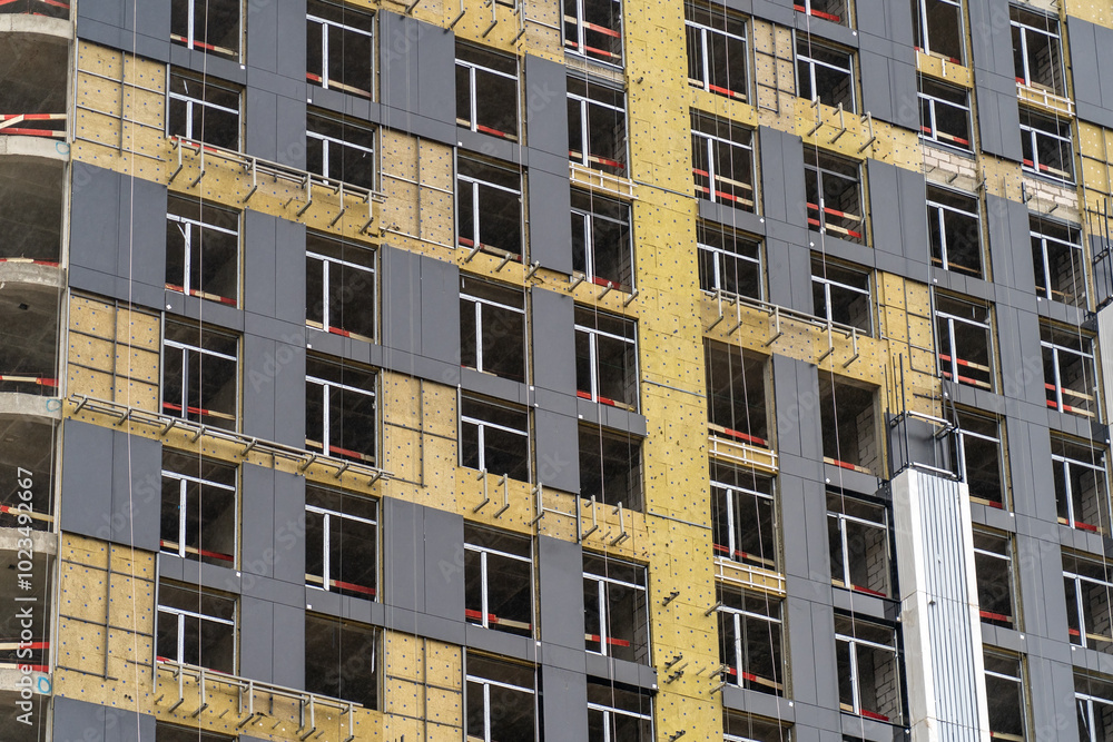 Poster workers are actively installing windows and cladding on a high-rise building under construction in a