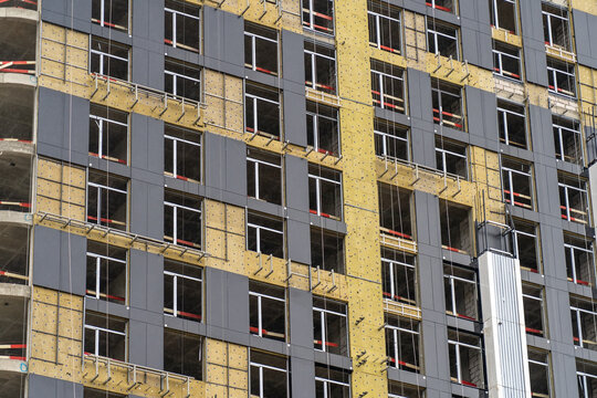 Workers are actively installing windows and cladding on a high-rise building under construction in a bustling city during the day