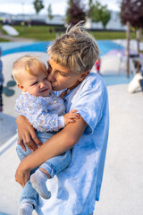 A delighted teen boy holds a smiling baby girl in his arms while enjoying a sunny day at a vibrant outdoor park filled with playful activities