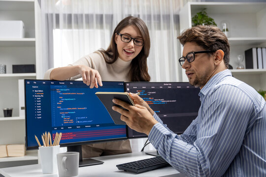 Woman colleague standing opposite to man programmer working on desk to discuss coding website software system project on two pc screen, comparing with typing full stack data prompt design. Postulate.
