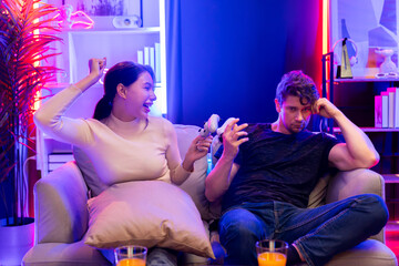 Smiling beautiful woman winner fighting gamer on video game beside loser man. Couple joyful of...