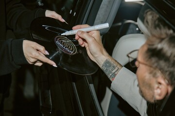 Close up on hand of successful music artist signing vinyl record with white marker through open car...
