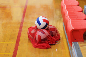 A Collection of Volleyballs Resting in a Red Net Beside the Court During a Practice Session at a Sports Facility