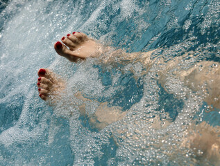 feet with red nail polish of a woman during hydrotherapy to stimulate blood circulation and...