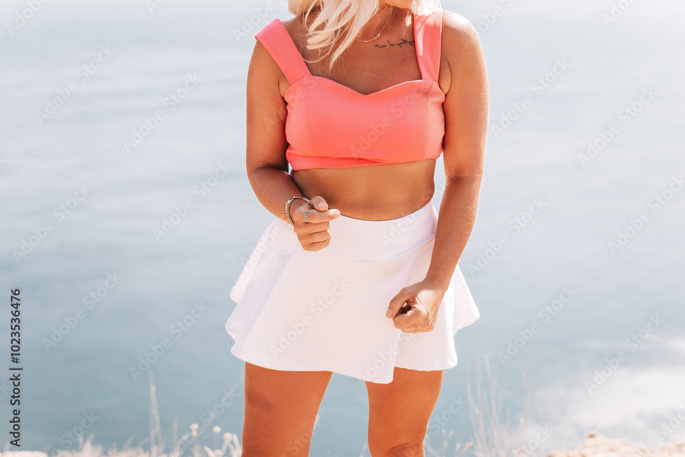 Poster A woman in a pink top and white skirt is standing on a hill overlooking a body of water.