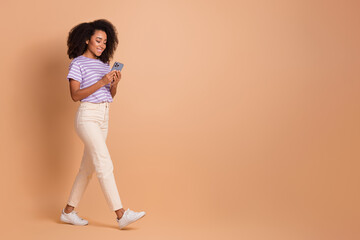 Full body portrait of pretty young girl use phone walk empty space wear t-shirt isolated on beige color background