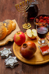 Challah, honey, pomegranate apple and wine with burning candles on a table with a menorah in honor...