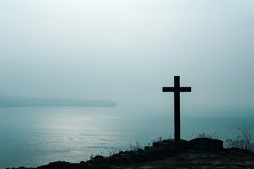Cross overlooking peaceful sea at dawn, serene landscape background
