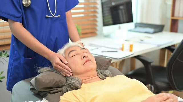 Physical therapist performing the Reiki treatment, channeling healing energy above mature woman head