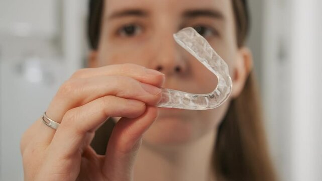 A teenager examines a transparent mouth guard. A girl shows a dental split to eliminate jaw clicking.