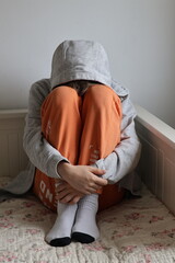 Broken boy sitting curled up on bed, bright colors © Gosia