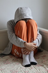 Broken boy sitting curled up on bed, bright colors © Gosia