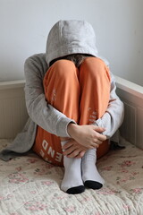 Broken boy sitting curled up on bed, bright colors © Gosia