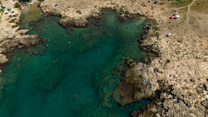 Aerial view of people bathing in the sea. The coast is rocky in this part of Salento, Puglia, Italy.