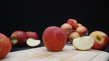 Macrography of apples displayed in various forms: whole, sliced, and within a glass bowl with black background. Each close-up shot captures the red colors of the apples on cutting board. Comestible.