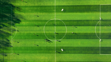 Aerial view of a soccer field with players and shadows. An aerial view of a soccer field with vivid green grass and a clearly marked center circle. © Iryna