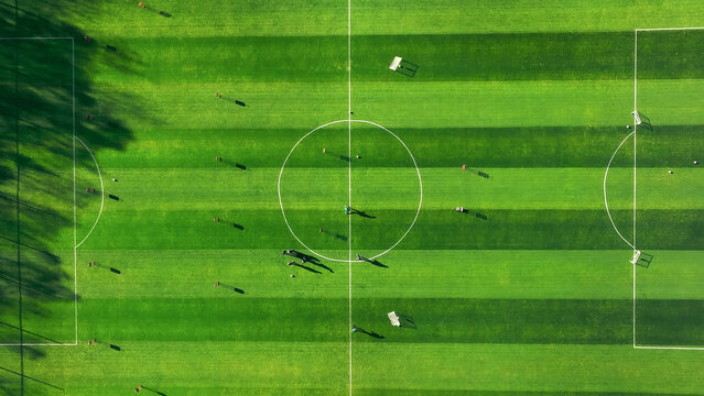 Aerial view of a soccer field with players and shadows. An aerial view of a soccer field with vivid green grass and a clearly marked center circle.