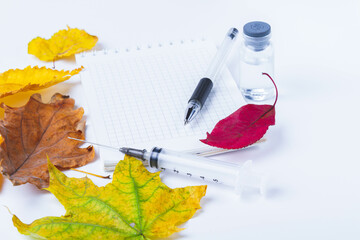 Vaccine and syringe are on table next to doctor's notebook and autumn leaves. Blank notebook for notes in doctor's office. Autumn vaccination.