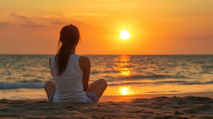 Fototapeta premium A woman sits on a beach watching the sunset.